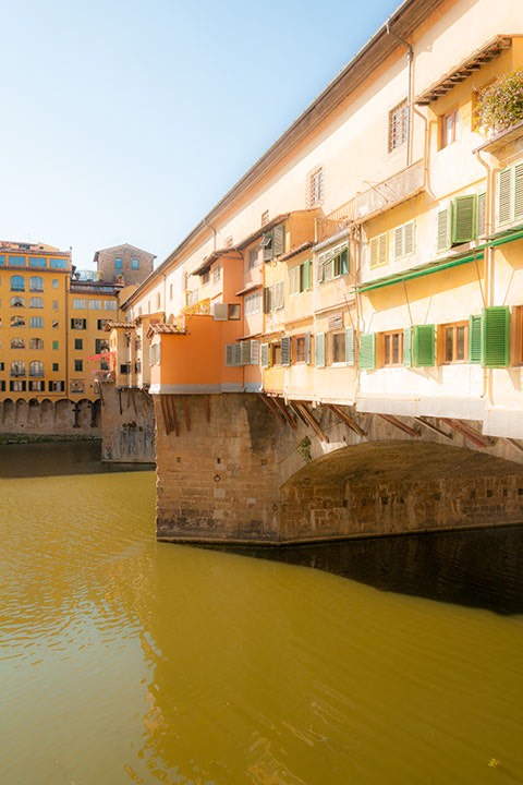 Florence's Ponte Vecchio bridge glows in the warm Tuscan sun as the green river slips by below