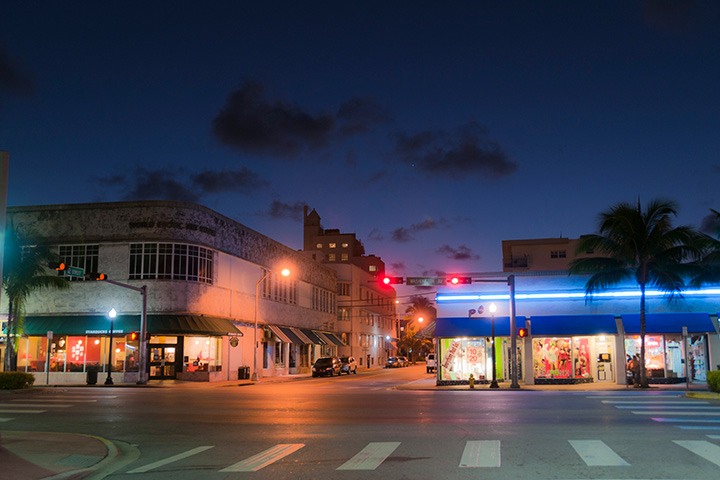 intersection of Washington Avenue and 12th Street in Miami Beach, with faint glow of receding sunset painting a gradient of blue across the sky as night draws on and the street lights glow