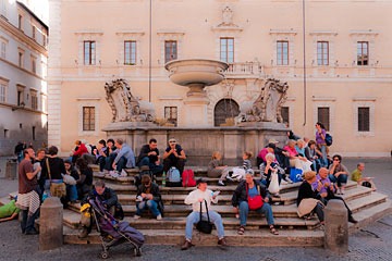 fountain in Rome piazza with people sitting on steps all around