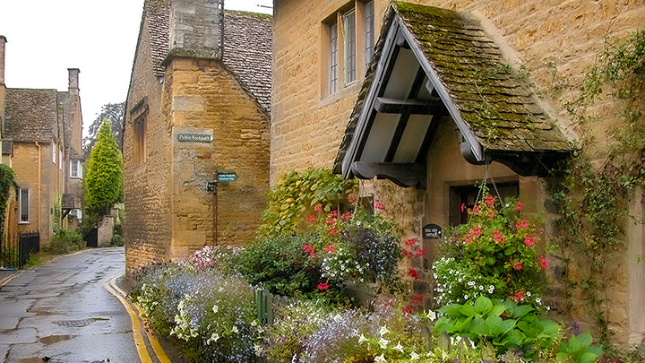 copious flowers of frontage garden spilling over fence along back street in Bourton-On-The-Water in England