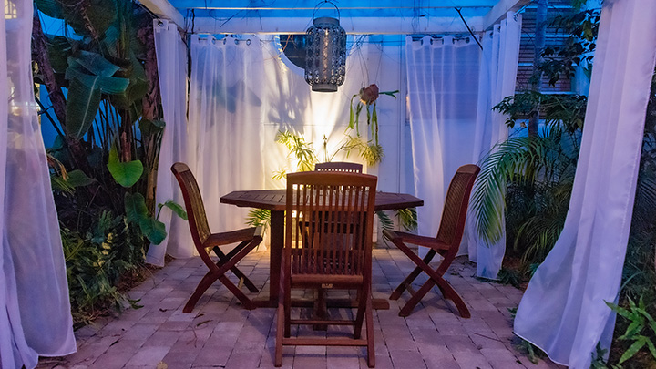 dinner garden courtyard with arbor over table and chairs with white curtains beyond