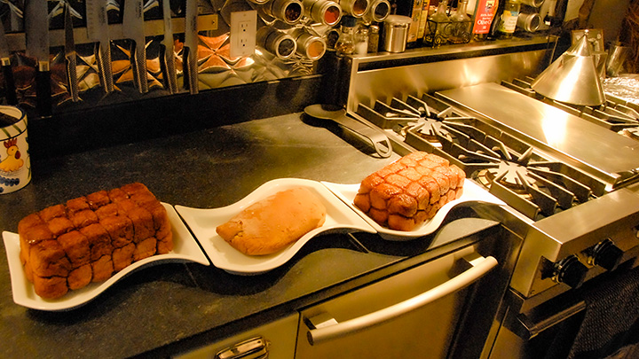 loaves of bread and monkey bread arranged on a soapstone countertop with pleated stainless steel wall beyond