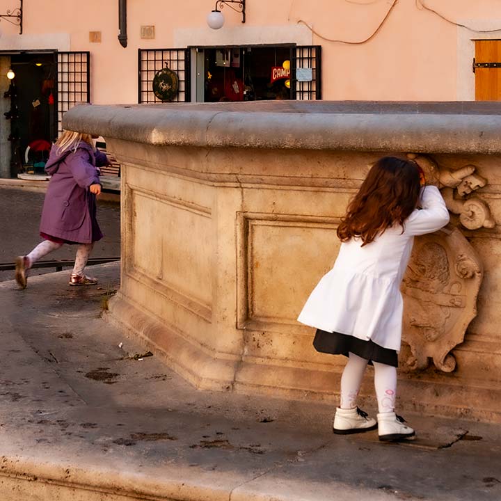 two little girls playing hide-and-seek in piazza in Rome