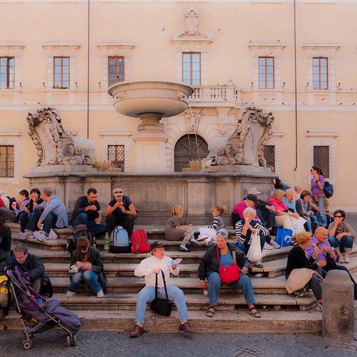 fountain in Rome piazza with people sitting on steps all around
