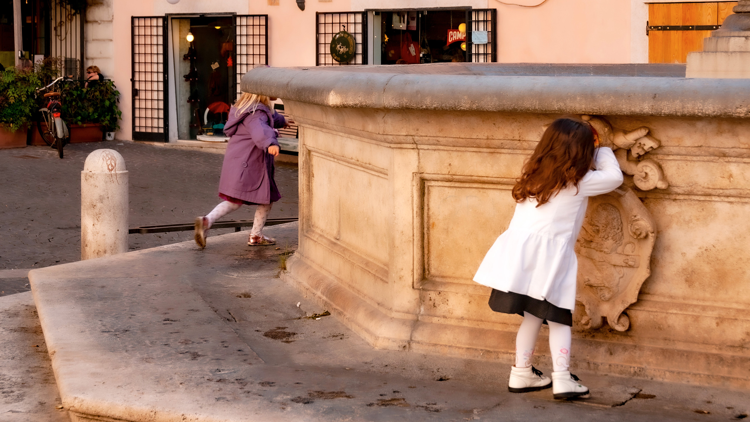two girls playing hide-and-seek on a Roman piazza