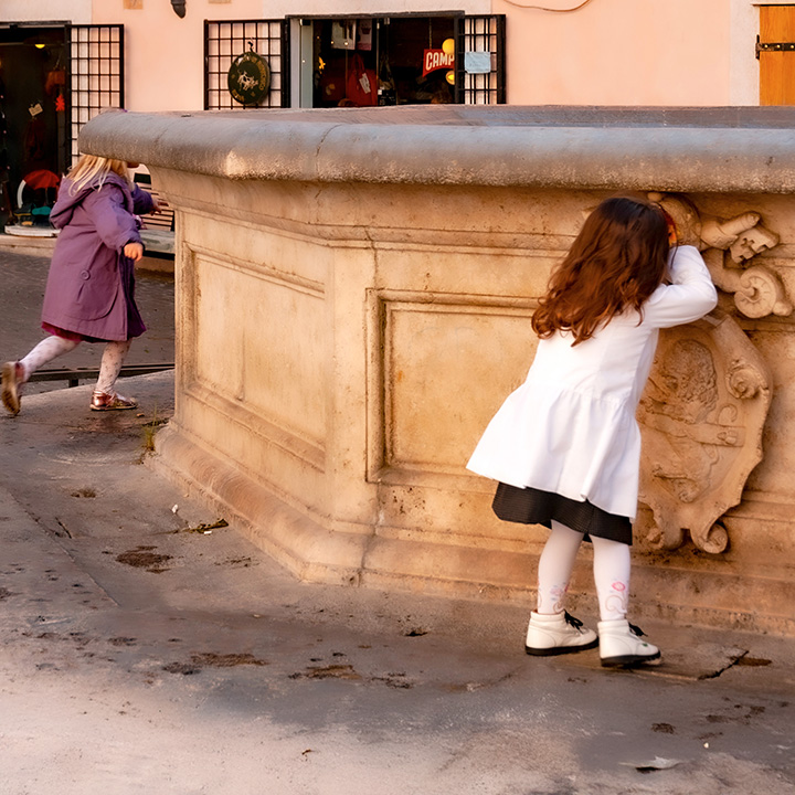 two girls playing hide-and-seek in a Rome piazza