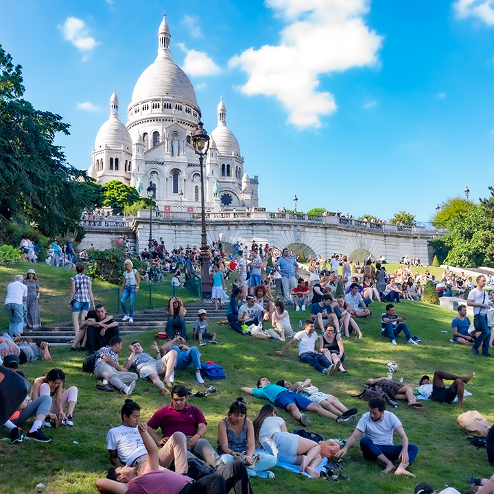 people sitting and laying on the grass just downhill from Sacre Coeur in Paris, enjoying a beautiful day