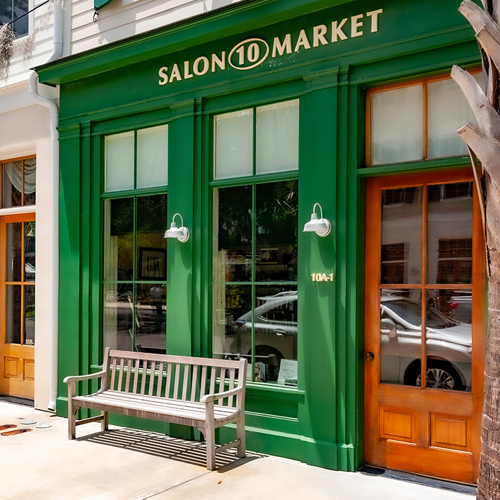 natural wood sidewalk bench centered on a pair of green-framed storefront windows on a Habersham shop